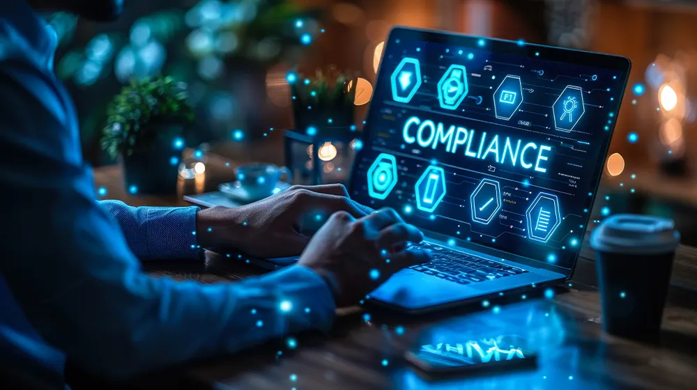 Image of a person typing on a laptop and checking a smartphone, with animated imagery related to compliance.